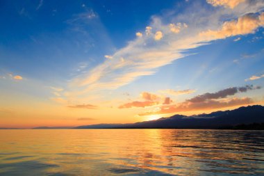 Denizde renkli bir gün batımı. Turuncu güneş ışınlarında dağ gölü. Kırgızistan, Issyk-Kul Gölü. doğal arkaplan