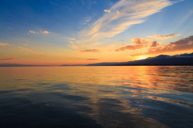 Denizde renkli bir gün batımı. Turuncu güneş ışınlarında dağ gölü. Kırgızistan, Issyk-Kul Gölü. doğal arkaplan