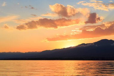 Denizde renkli bir gün batımı. Turuncu güneş ışınlarında dağ gölü. Kırgızistan, Issyk-Kul Gölü. doğal arkaplan