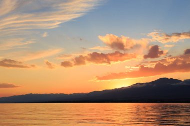 Denizde renkli bir gün batımı. Turuncu güneş ışınlarında dağ gölü. Kırgızistan, Issyk-Kul Gölü. doğal arkaplan