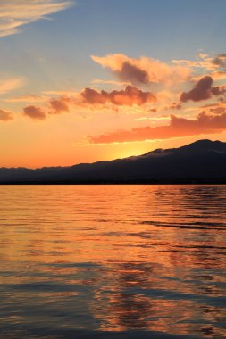 Denizde renkli bir gün batımı. Turuncu güneş ışınlarında dağ gölü. Kırgızistan, Issyk-Kul Gölü. doğal arkaplan
