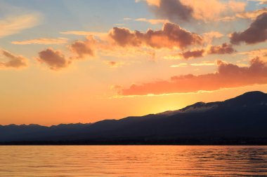 Denizde renkli bir gün batımı. Turuncu güneş ışınlarında dağ gölü. Kırgızistan, Issyk-Kul Gölü. doğal arkaplan