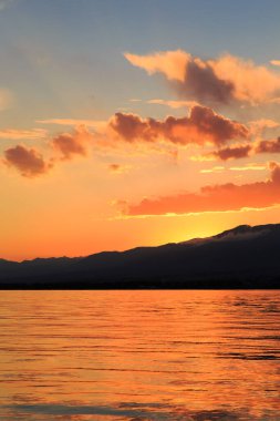 Denizde renkli bir gün batımı. Turuncu güneş ışınlarında dağ gölü. Kırgızistan, Issyk-Kul Gölü. doğal arkaplan