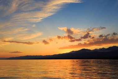 Dağların üzerinde renkli deniz plajı. Gün doğumu. Derin mavi gökyüzü ve güneş ışınları. Doğal arka plan. Turuncu güneşin ışınlarında parlak gökyüzü.