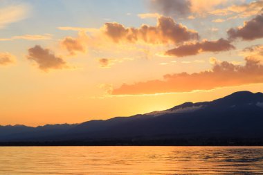 Denizde renkli bir gün batımı. Turuncu güneş ışınlarında dağ gölü. Kırgızistan, Issyk-Kul Gölü. doğal arkaplan