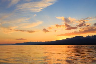 Denizde renkli bir gün batımı. Turuncu güneş ışınlarında dağ gölü. Kırgızistan, Issyk-Kul Gölü. doğal arkaplan