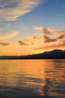Denizde renkli bir gün batımı. Turuncu güneş ışınlarında dağ gölü. Kırgızistan, Issyk-Kul Gölü. doğal arkaplan