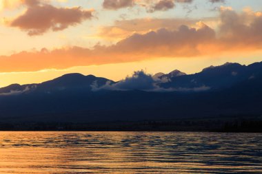 Denizde renkli bir gün batımı. Turuncu güneş ışınlarında dağ gölü. Kırgızistan, Issyk-Kul Gölü. doğal arkaplan
