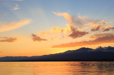 Denizde renkli bir gün batımı. Turuncu güneş ışınlarında dağ gölü. Kırgızistan, Issyk-Kul Gölü. doğal arkaplan