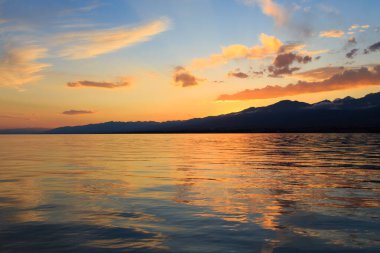 Denizde renkli bir gün batımı. Turuncu güneş ışınlarında dağ gölü. Kırgızistan, Issyk-Kul Gölü. doğal arkaplan