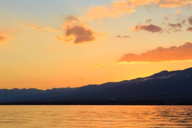 Dağların üzerinde renkli deniz plajı. Gün doğumu. Derin mavi gökyüzü ve güneş ışınları. Doğal arka plan. Turuncu güneşin ışınlarında parlak gökyüzü.