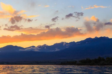 Denizde renkli bir gün batımı. Turuncu güneş ışınlarında dağ gölü. Kırgızistan, Issyk-Kul Gölü. doğal arkaplan