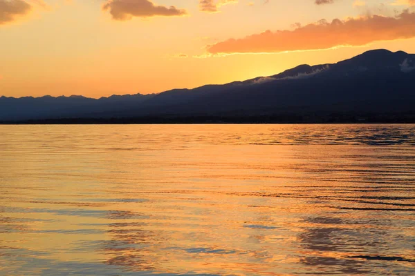 Denizde renkli bir gün batımı. Turuncu güneş ışınlarında dağ gölü. Kırgızistan, Issyk-Kul Gölü. doğal arkaplan