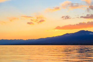 Denizde renkli bir gün batımı. Turuncu güneş ışınlarında dağ gölü. Kırgızistan, Issyk-Kul Gölü. doğal arkaplan