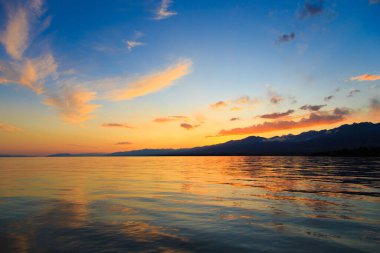 Denizde renkli bir gün batımı. Turuncu güneş ışınlarında dağ gölü. Kırgızistan, Issyk-Kul Gölü. doğal arkaplan