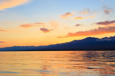 Dağların üzerinde renkli deniz plajı. Gün doğumu. Derin mavi gökyüzü ve güneş ışınları. Doğal arka plan. Turuncu güneşin ışınlarında parlak gökyüzü.