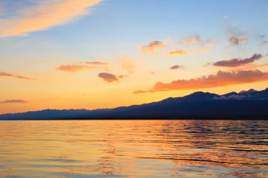 Deniz ve dağların üzerinde güzel bulutlu gün batımı. Turuncu güneşin ışınlarında parlak bir gökyüzü. Doğal