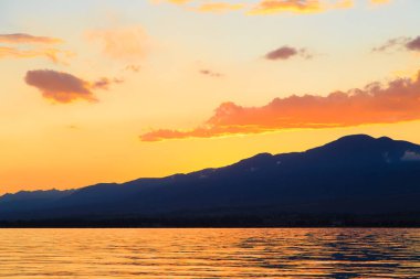 Denizde renkli bir gün batımı. Turuncu güneş ışınlarında dağ gölü. Kırgızistan, Issyk-Kul Gölü. doğal arkaplan