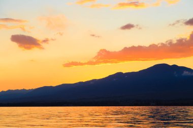 Dağların üzerinde renkli deniz plajı. Gün doğumu. Derin mavi gökyüzü ve güneş ışınları. Doğal arka plan. Turuncu güneşin ışınlarında parlak gökyüzü.