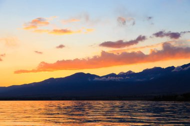 Denizde renkli bir gün batımı. Turuncu güneş ışınlarında dağ gölü. Kırgızistan, Issyk-Kul Gölü. doğal arkaplan
