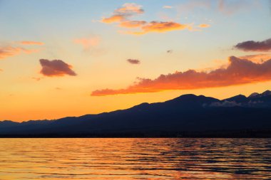 Denizde renkli bir gün batımı. Turuncu güneş ışınlarında dağ gölü. Kırgızistan, Issyk-Kul Gölü. doğal arkaplan