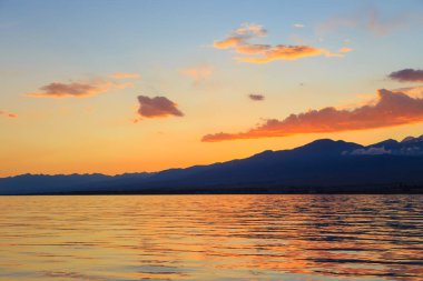 Deniz ve dağların üzerinde güzel bulutlu gün batımı. Turuncu güneşin ışınlarında parlak bir gökyüzü. Doğal