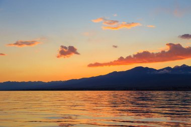 Deniz ve dağların üzerinde güzel bulutlu gün batımı. Turuncu güneşin ışınlarında parlak bir gökyüzü. Doğal
