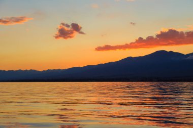 Denizde renkli bir gün batımı. Turuncu güneş ışınlarında dağ gölü. Kırgızistan, Issyk-Kul Gölü. doğal arkaplan