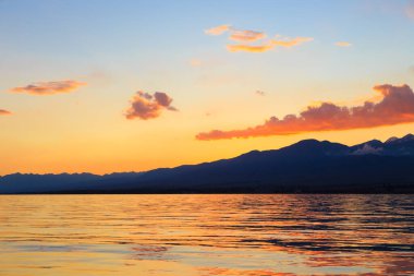 Denizde renkli bir gün batımı. Turuncu güneş ışınlarında dağ gölü. Kırgızistan, Issyk-Kul Gölü. doğal arkaplan