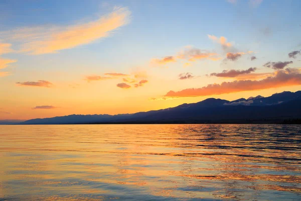 Denizde renkli bir gün batımı. Turuncu güneş ışınlarında dağ gölü. Kırgızistan, Issyk-Kul Gölü. doğal arkaplan