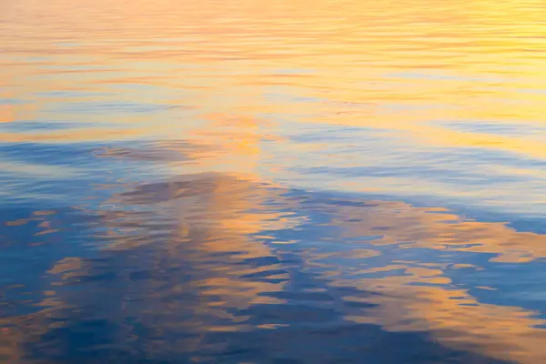 Clear water texture in blue and orange. Background of the ocean and the sea backlit by the sun.