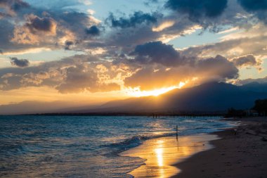 Denizde renkli bir gün batımı. Turuncu güneş ışınlarında dağ gölü. Kırgızistan, Issyk-Kul Gölü. Doğal arka plan. Peyzaj