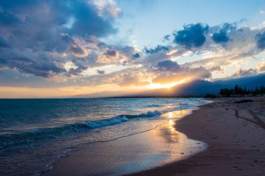 Denizde renkli bir gün batımı. Turuncu güneş ışınlarında dağ gölü. Kırgızistan, Issyk-Kul Gölü. Doğal arka plan. Peyzaj