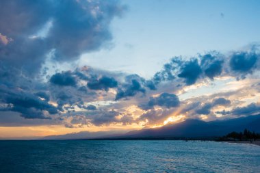 Denizde renkli bir gün batımı. Turuncu güneş ışınlarında dağ gölü. Kırgızistan, Issyk-Kul Gölü. Doğal arka plan. Peyzaj