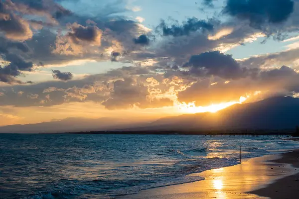 Denizde renkli bir gün batımı. Turuncu güneş ışınlarında dağ gölü. Kırgızistan, Issyk-Kul Gölü. Doğal arka plan. Peyzaj