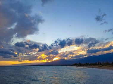 Denizde renkli bir gün batımı. Turuncu güneş ışınlarında dağ gölü. Kırgızistan, Issyk-Kul Gölü. Doğal arka plan. Peyzaj