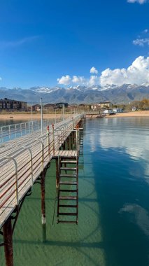 Deniz kıyısındaki ahşap iskele. Dağlar ve berrak su. Issyk-Kul Gölü