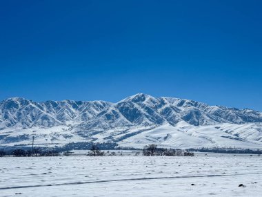 Kırgızistan dağlarında karlı bir ovada ayak izleri. Açık gökyüzü ve karla kaplı zirveler sakin ve engin boşluklardan oluşan bir atmosfer yaratır.