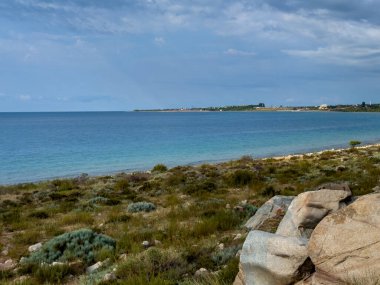 Issyk-Kul 'un kayalık kıyı manzarası. Çalı bitki örtüsü ve mavi gökyüzü. Kırgızistan 'da turistler ve gezginler için doğal bir yer