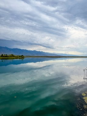 Yeşil vadiler ve görkemli dağlarla çevrili sessiz bir dağ gölü Issyk-Kul. Kırgızistan 'da turizm ve huzurlu dinlenme için mükemmel bir yer.