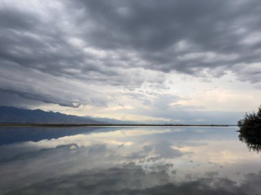 Issyk-Kul gölünün sakin suları dramatik bulutları ve dağları yansıtır. Kırgızistan 'daki doğal bir vahada sessizlik ve sükunet..