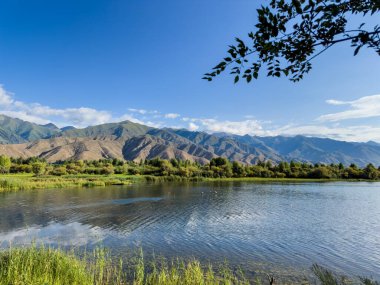 Yeşil vadiler ve görkemli dağlarla çevrili sessiz bir dağ gölü Issyk-Kul. Kırgızistan 'da turizm ve huzurlu dinlenme için mükemmel bir yer.