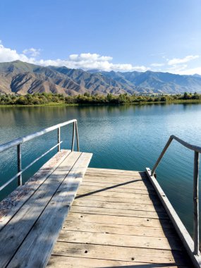 Issyk-Kul Gölü 'nde dağları gören ahşap bir iskele. Rahatlamak ve Kırgızistan 'ın doğal manzaralarının tadını çıkarmak için güzel bir yer..