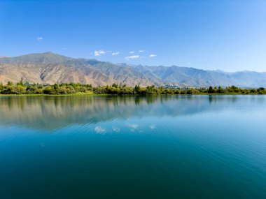 Arka planda görkemli dağlarla Issyk-Kul gölünün sakin su yüzeyi. Kırgızistan 'ın güzel doğal manzarası.