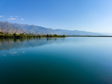 Arka planda görkemli dağlarla Issyk-Kul gölünün sakin su yüzeyi. Kırgızistan 'ın güzel doğal manzarası.