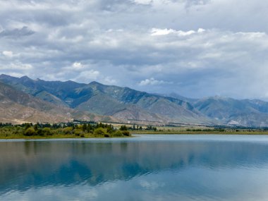 Arka planda görkemli dağlarla Issyk-Kul gölünün sakin su yüzeyi. Kırgızistan 'ın güzel doğal manzarası.