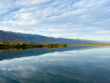 Issyk-Kul gölünün sakin suları dramatik bulutları ve dağları yansıtır. Kırgızistan 'daki doğal bir vahada sessizlik ve sükunet..