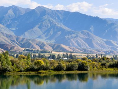 Kabarık bulutlarla dolu bir gökyüzünün altında yeşil ve kahverengiye boyanmış görkemli dağların manzarası. Engebeli arazi, yukarıdaki dingin gökyüzü ile çok güzel tezat oluşturuyor.