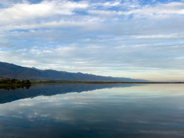Yeşil vadiler ve görkemli dağlarla çevrili sessiz bir dağ gölü Issyk-Kul. Kırgızistan 'da turizm ve huzurlu dinlenme için mükemmel bir yer.