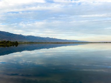 Issyk-Kul gölünün sakin suları dramatik bulutları ve dağları yansıtır. Kırgızistan 'daki doğal bir vahada sessizlik ve sükunet..